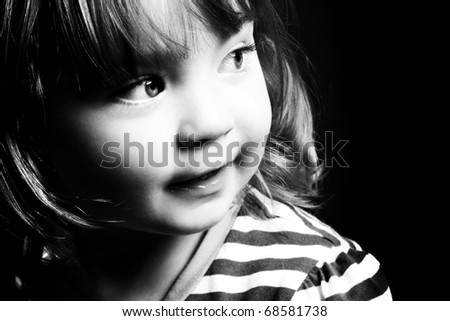 An adorable little girl looking to the light in front of a black background. Black and white.