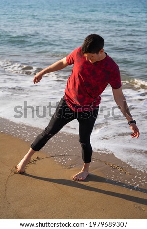 Man drawing a circle with his foot on the seashore. He is barefoot and his trousers are rolled up. It is a sunny day and the sea is blue. He is balancing on one leg. Les Marines, Denia. Photo stock © 