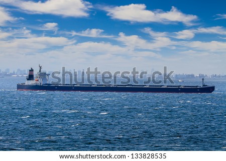 300 meter long supersize bulk transport ship travels across a large hazy harbor.