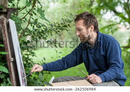 Male artist on painting on canvas in outdoor. Fine art artist. Plein-air.