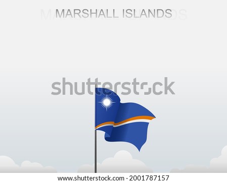The Marshall Islands flag flutters on a pole that stands tall against a white sky