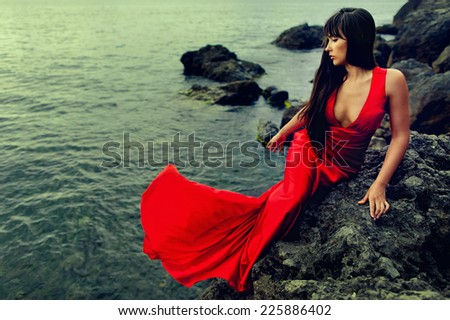 brunette lady with long hair in red dress on the rock seashore, near the sea, movement