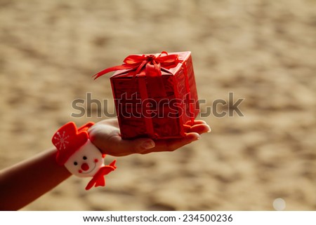 new year present gift in red box in hand on the beach in tropics / christmas gift in red box on the beach