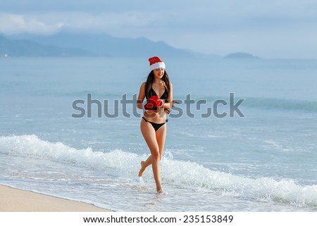 santa girl in bikini on the beach  resort  with present. Happy new year girl in bikini on the beach running with gift, delivery christmas gift / santa girl with christmas present on the beach