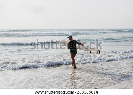 woman with surfing board on the beach in the morning back view