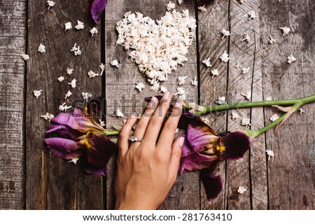heart shape white lilac flowers and violet irises with on hand proposal wedding ring on vintage wood table