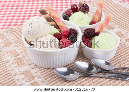 Chocolate chip and lemon ice cream with waffle sticks and mixed frozen fruits in white bowls.