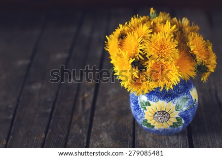 Bright natural dandelion summer bouquet on a dark wooden rustic surface in a blue vase indoors