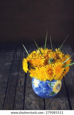 Bright natural dandelion spring bouquet on a dark wooden rustic surface in a blue vase indoors