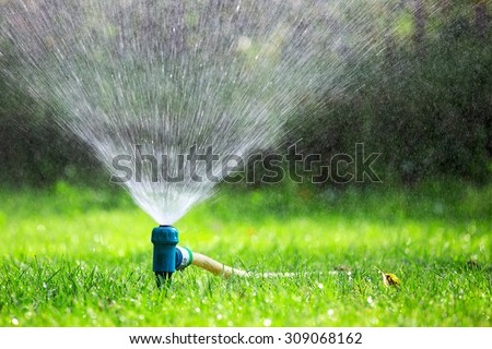 Lawn sprinkler spraying water over grass in garden on a hot summer day