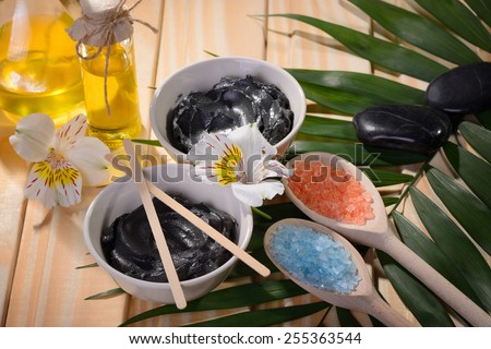 black clay from the Dead sea  two bowls for procedures stones for massage bottle with butter buds of flowers on the table color birch and fern and wooden sticks two wooden spoons salt blue and orange