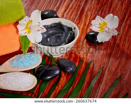medical black clay in a bowl on a red wooden table sea salt in a spoon and two towels flowers