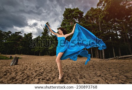 Slim girl in blue flowing dress against the sky