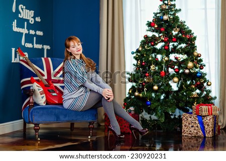Pregnant girl in the grey dress on the background of the Christmas tree sits on the armchair