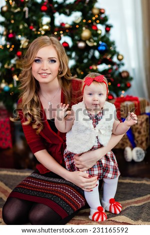 Very cute mother and daughter in red on the background of the Christmas tree