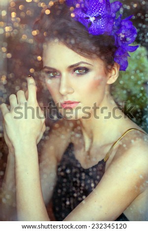 Sensual beautiful brunette behind the glass, through which drain water drops, close up