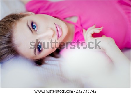 Portrait of a beautiful sensual girl in a pink dress lying on the bed