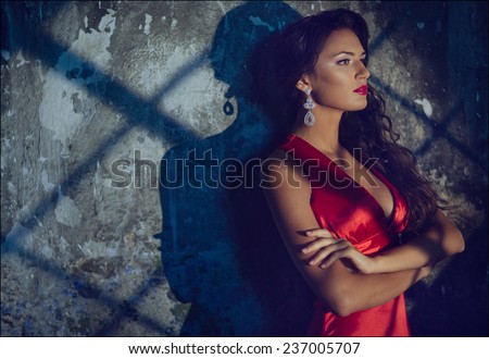 Portrait of a sensual sexy beautiful curly girl in a red dress against the wall with the shadows, close up