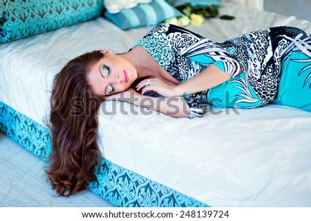 portrait of a very beautiful pregnant girl with gorgeous brown hair and eyes closed in a blue dress lying on the bed and sleeping