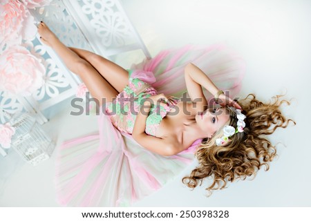 Very beautiful sensual girl with curly blond hair and a wreath of delicate spring flowers, lying on the background of large pink flowers and white cells