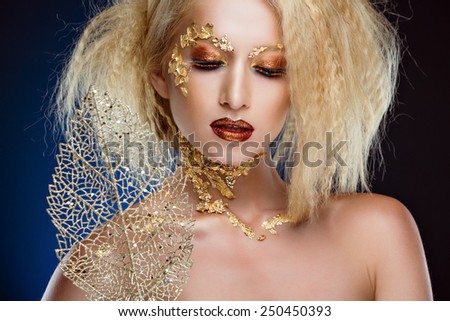 Portrait of a glamorous blonde girl with beautiful Golden makeup and gold foil on a blue background in Studio, close-up