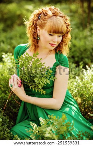 portrait of a beautiful curly haired pregnant girl in a green dress sitting in the grass in the forest