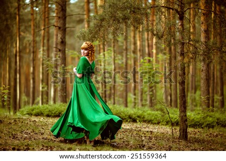 Portrait of a beautiful curly haired pregnant girls flying in a green dress in the woods among the pines