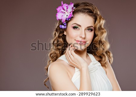 A very delicate portrait of a cute smiling girl with brown curly hair and natural makeup, on a gray background in Studio