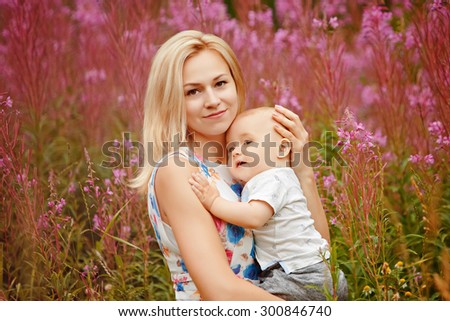 Beautiful slim blonde mom hugs adorable little boy , on the background of grass fireweed in the summer