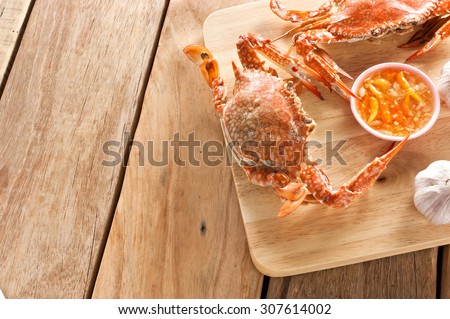 Two boiled crabs on wooden cutting board with seafood sauce.
