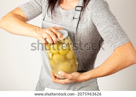 A caucasian woman chef wearing apron is trying to open a stubborn jar lid. She uses force to unscrew the lid in kitchen. Concept image for pickling tomatoes and gherkins and difficulty in opening lids Photo stock © 