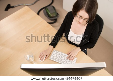 A woman works from home on a computer with a vacuum cleaner in the background
