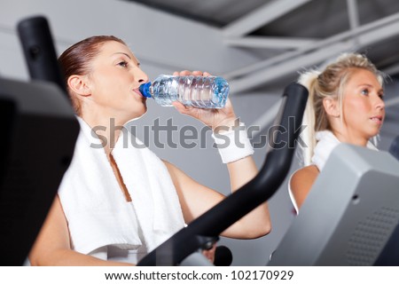 young woman drinking water while exercising in gym