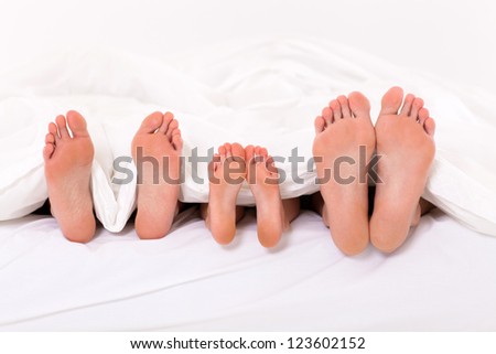 happy family of three lying under duvet on bed