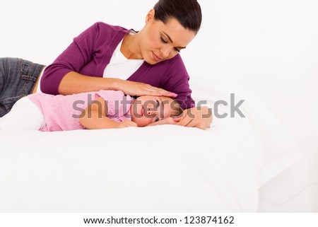 caring mother comforting crying baby girl on bed