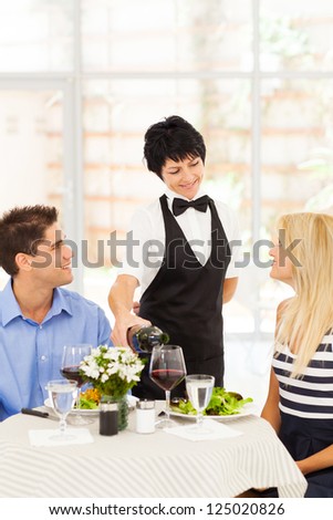 friendly mature waitress serving wine to diners in restaurant
