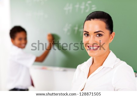 pretty elementary school teacher and student in front of chalkboard