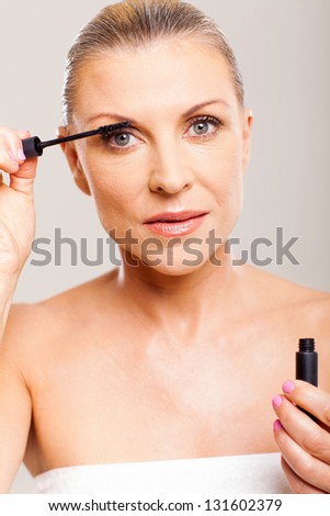 pretty mid age woman putting mascara on her eyelashes