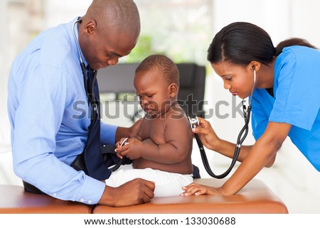 female african medical assistant examining a baby together with doctor