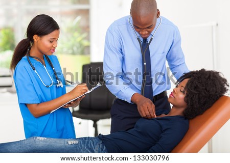 african american doctor and nurse examining female patient on examining couch