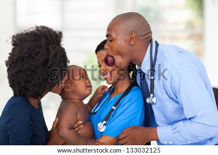 funny african male doctor cheering up sick baby with mother and female nurse