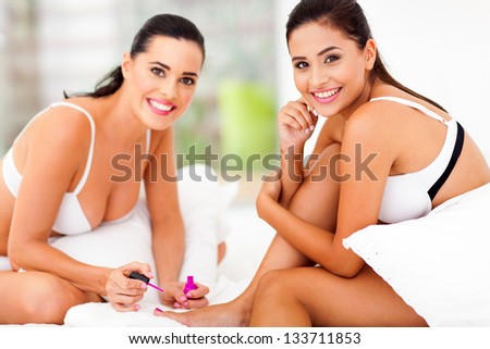 two happy lady friends doing pedicure on bed at home