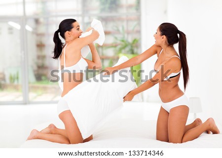 two girl friends having pillow fight in bedroom