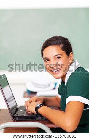 portrait of cheerful female middle school student using laptop in classroom