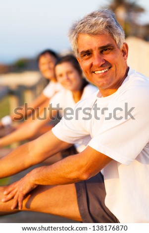 middle aged man stretching before exercise with family at the beach