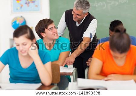 senior high school teacher talking to student in classroom