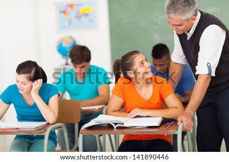smiling senior high school teacher talking to student in classroom