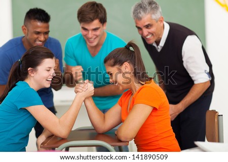 cheerful female high school students playing arm wrestling in classroom