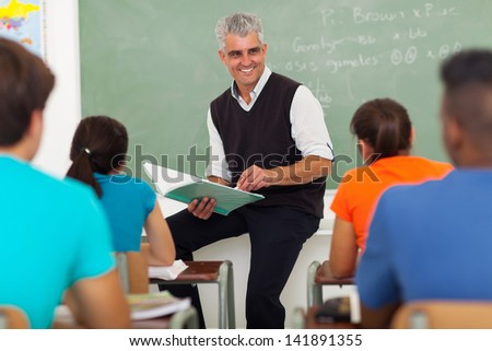 smiling senior teacher teaching group of high school students in classroom