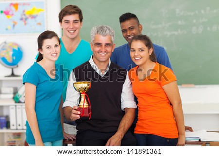 senior teacher and group of high school students holding trophy in classroom